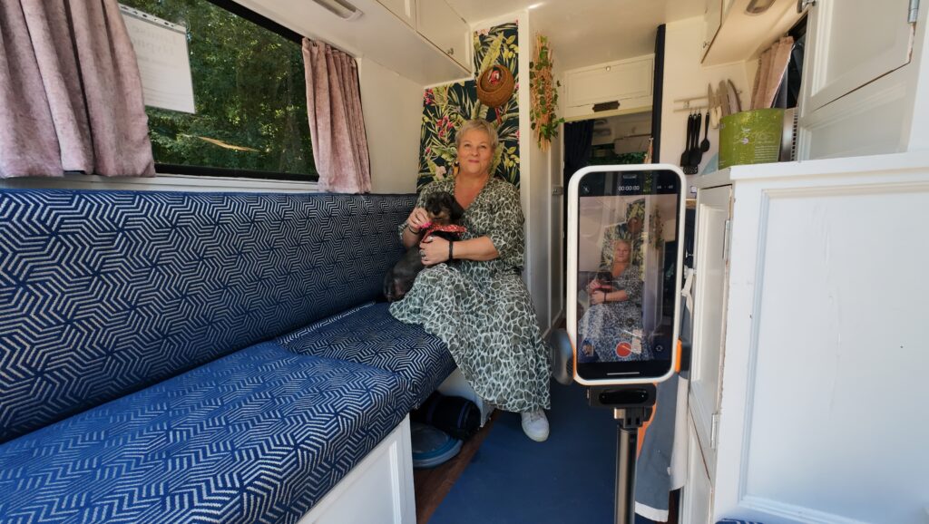 iPhone on Tripod filming social media content for hypnotherapist in caravan wearing a long green dress and has a dog with a little dachshund on her lap